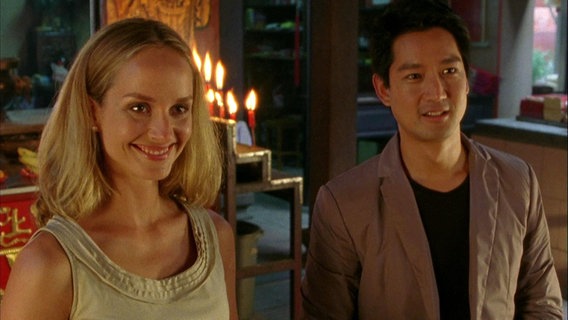 Eine blonde Frau und ein asiatischer Mann stehen nebeneinander und lächeln in die Kamera. © Screenshot 