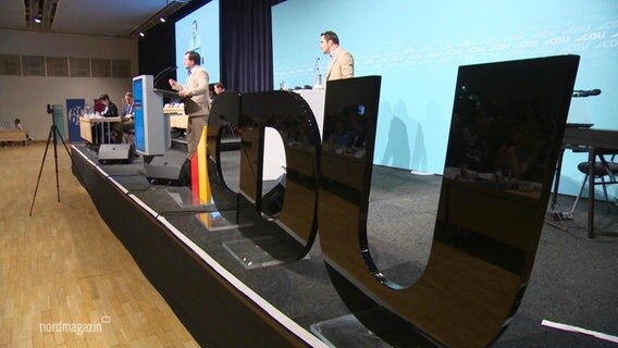 Auf einer Bühne stehen neben einem Rednerpult große, schwarze Lettern, die das Wort "CDU" bilden. © Screenshot 