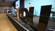 Auf einer Bühne stehen neben einem Rednerpult große, schwarze Lettern, die das Wort "CDU" bilden. © Screenshot 