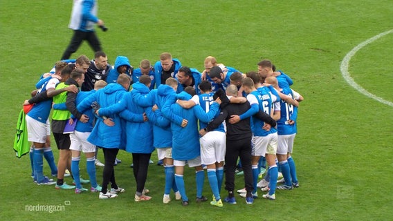 Bei einem Spiel stehen die Spieler von Hansa Rostock besprechend in einem Kreis Arm in Arm. © Screenshot 