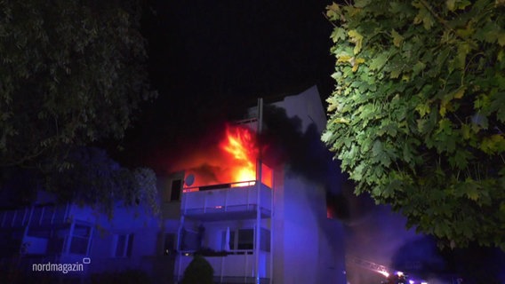 Auf einem Balkon eines bei Nacht von blauem Polizeilicht angestrahlten Mehrfamilienhauses brennt einen großes Feuer. © Screenshot 