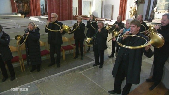 Mehrere Jagdhornbläser spielen ihre Instrumente in einer Kirche. © Screenshot 