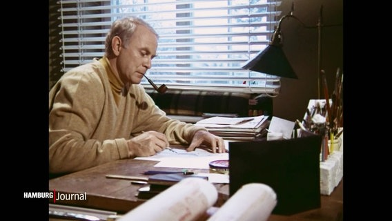 Vicco von Bülow alias Loriot bei der Arbeit: Mit einer Pfeife im Mund sitzt er am Schreibtisch und zeichnet. © Screenshot 