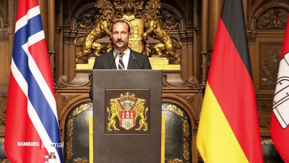 Kronprinz Haakon im Rathaus am Rednerpult, links im Bild die norwegische und rechts im Bild die deutsche Nationalflagge. © Screenshot 