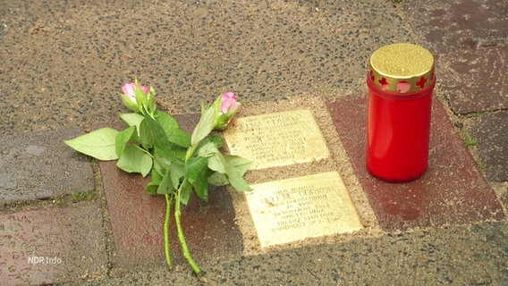 Blumen und eine Kerzen neben zwei Stolpersteinen. © Screenshot 