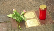 Blumen und eine Kerzen neben zwei Stolpersteinen. © Screenshot 