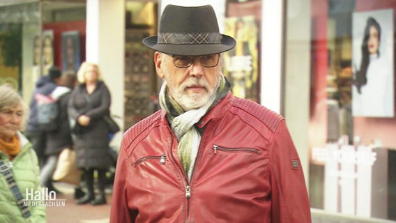 Eine Person mit Bart, Hut und roter Lederjacke in einer Fußgängerzone. © Screenshot 