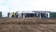 Auf einem Bauplatz stecken mehrere Spaten im Boden, dahinter haben sich mehrere Menschen versammelt. © Screenshot 