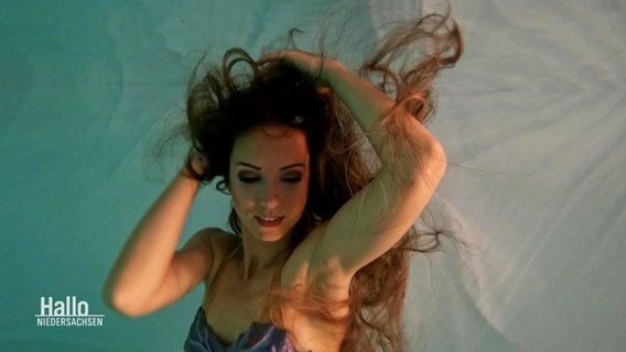 Eine Frau modellt als Meerjungfrau verkleidet unter Wasser. © Screenshot 