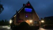 Blick bei Nacht auf ein modernes, ehemaliges Kirchengebäude das nun als Gruselmuseum bunt beleuchtete Fenster aufweist. © Screenshot 