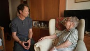 Moderator Jo Hiller unterhält sich mit einer älteren Dame, die in einem Ohrensessel in einem Apartment eines Pflegeheims sitzt. © Screenshot 
