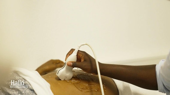 Bei einem Patienten mit dunkler Hautfarbe wird eine Ultraschalluntersuchung auf dem Bauch gemacht. © Screenshot 