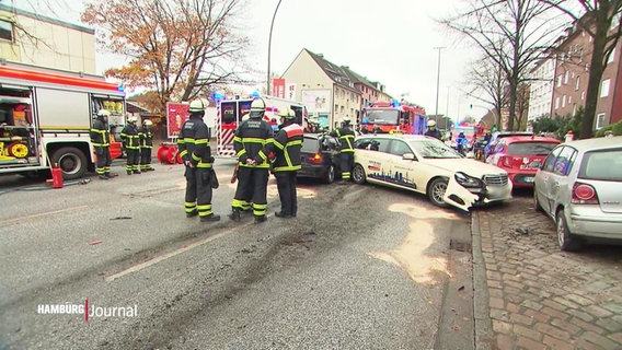 Auf einer mehrspurigen Straße sind Rettungskräfte der Feuerwehr dabei eine Unfallstelle mit mehreren Fahrzeugen, unter anderem ein Taxi, abzusichern. © Screenshot 