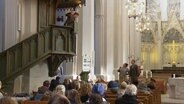 In einer Kirche spielen Darstellende ein Theaterstück in dem ein Schauspieler von der Kanzel spricht. © Screenshot 