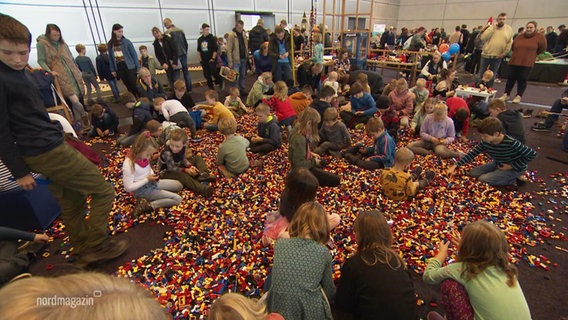 Viele Kinder spielen in einer Messehalle in einem Haufen Lego-Steine. © Screenshot 