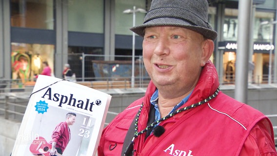 Joachim Weber verkauft das Straßenmagazin "Asphalt" auf der Straße, er lächelt. © Screenshot 