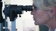Eine Frau blickt in ein medizinisches Augeninstrument. © Screenshot 