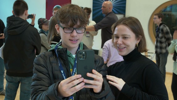 Eine NDR Volonatärin erklärt einem Schüler etwas an einem Smartphone während des Jugendmedientages im Landesfunkhaus Schwerin. © Screenshot 
