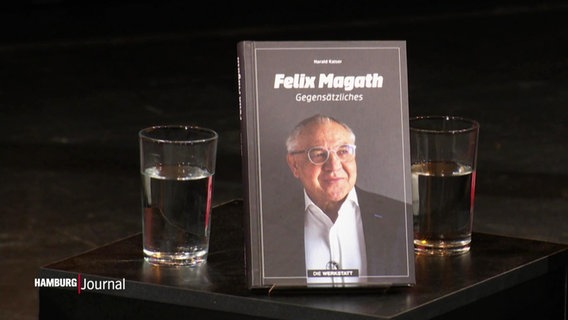 Die Biografie von Felix Magath steht auf einem Tisch zwischen zwei Wassergläsern. © Screenshot 