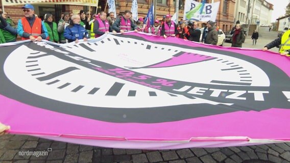 Menschen halten ein großes Protestplakat. © Screenshot 