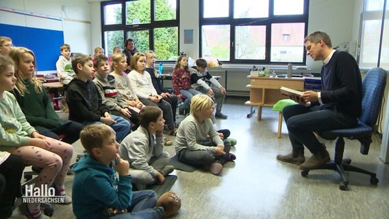 Arne-Torben Voigts liest in der Grundschule Bredenbeck Schülern etwas vor. © Screenshot 