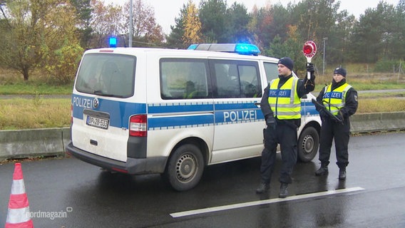 Ein Polizist streckt eine rote Winkerkelle in die Höhe. © Screenshot 