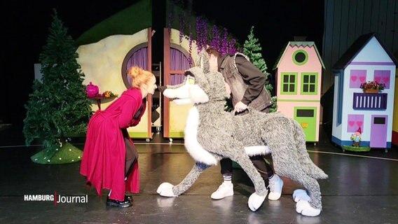 Szene aus einer Inszenierung von Rotkäppchen: eine Frau streitet sich mit einer großen Wolfspuppe. © Screenshot 