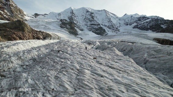 Ein Mensch läuft über ein großes Eisfeld zwischen Bergen. © Screenshot 