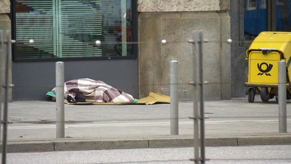 Ein obdachlose Person liegt auf der Straße unter einer Decke. © Screenshot 