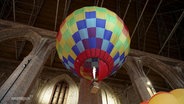 Ein kleiner Heißluftballon fliegt unter die Decke einer Kirche. © Screenshot 