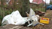 An einem Gartenzaun lehnt viel Haushaltsschrott, der durch ein Hochwasser entstanden ist. © Screenshot 