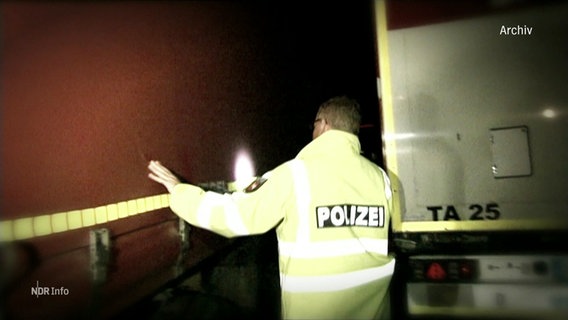 Ein Polizist untersucht eine LKW-Plane bei Nacht. © Screenshot 