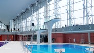 In einer modernen Schwimmhalle sind zwei Sprungtürme zu sehen. © Screenshot 