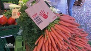 Über Karotten liegt auf einem Wochenmarkt eine Papiertüte mit der Aufschrift "Stopp Gewalt gegen Frauen". © Screenshot 