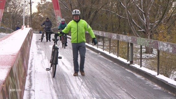 Ein Mann schiebt sein Fahrrad eine glatte Brücke hinunter. © Screenshot 