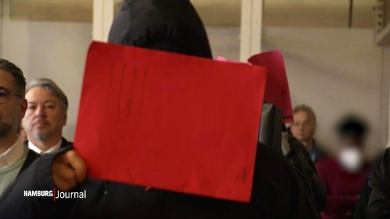 Einer der verurteilten Täter hält sich eine rote Mappe vor sein Gesicht. © Screenshot 