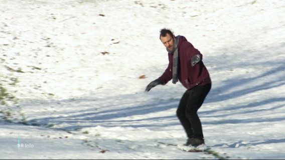 Mann fährt mit einem Board einen kleinen verschneiten Hügel runter. © Screenshot 