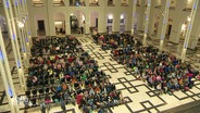 Kinder sitzen in einem großen Hörsaal. © Screenshot 