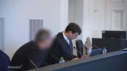 Eine Anklagebank in einem Gericht, der Angeklagte ist verpixelt zu sehen. © Screenshot 