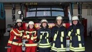 Fünf junge Menschen stehen in Arbeitskleidung vor einem Feuerwehrfahrzeug. Sie haben die Arme vor der Brust gekreuzt und sehen freundlich und entschlossen in die Kamera. © Screenshot 
