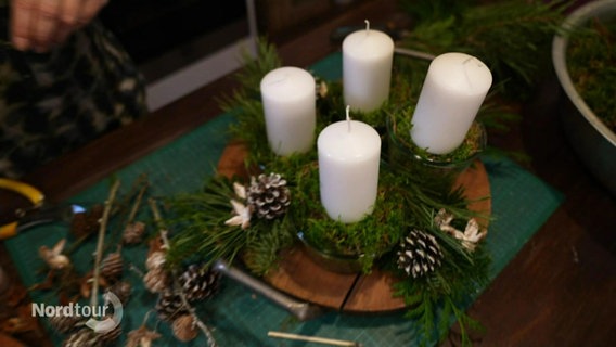 Ein Adventskrankz mit weißen Kerzen, Moos und Tannenzapfen. © Screenshot 