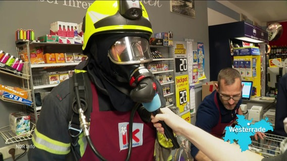 Ein Feuerwehrmann in Arbeitsmontur, Helm und Atemgerät an einer Supermarktkasse. © Screenshot 