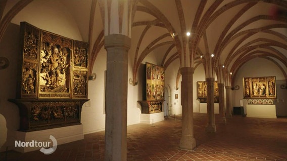 Kreuzgang im St. Annen Museum in Lübeck. An den Wänden hängen geschnitzte Altäre. © Screenshot 