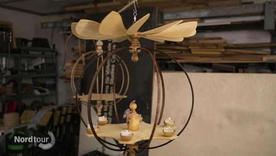 In der Werkstatt: Eine Hängepyramide, zusammengesetzt aus verschiedenen Rundstäben und einer Platte für Figuren und Kerzen, dsrüber ein Propeller aus Holz. © Screenshot 