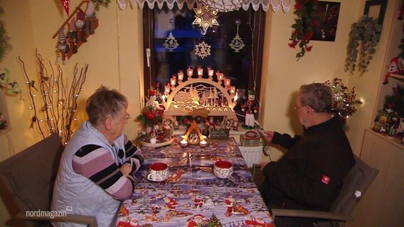 Ein älteres Paar sitzt an einem Esstisch in einem geschmückten Zimmer. © Screenshot 
