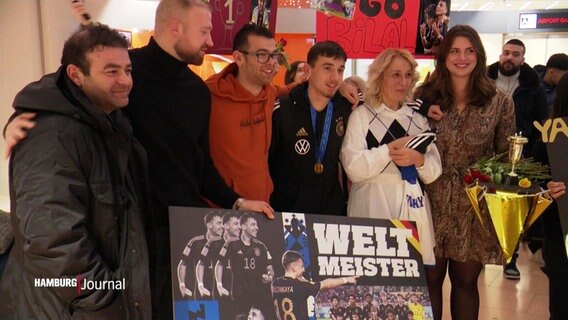 Empfangskomitee am Hamburger Flughafen, u.a. mit einem Schild, auf dem Weltmeister steht. © Screenshot 