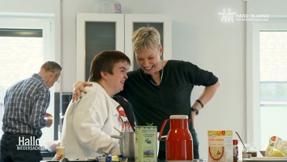 Eine Frau ohne und eine Frau mit Behinderung lachen gemeinsam in einer Küche. © Screenshot 