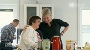 Eine Frau ohne und eine Frau mit Behinderung lachen gemeinsam in einer Küche. © Screenshot 