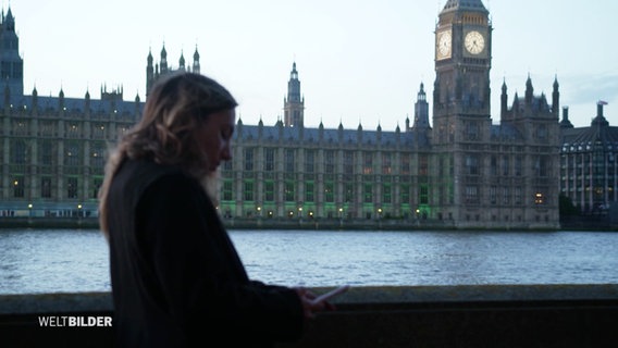Eine junge Frau steht an der Themse – im Hintergrund ist das Londoner Regierungsviertel zu sehen. © Screenshot 