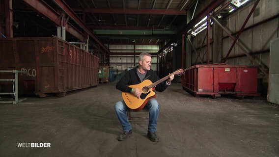 Ein Mann sitzt in einer Fabrikhalle und spielt Gitarre © Screenshot 